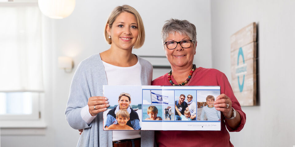 Zwei Frauen halten ein geöffnetes Fotobuch mit Familienfotos.
