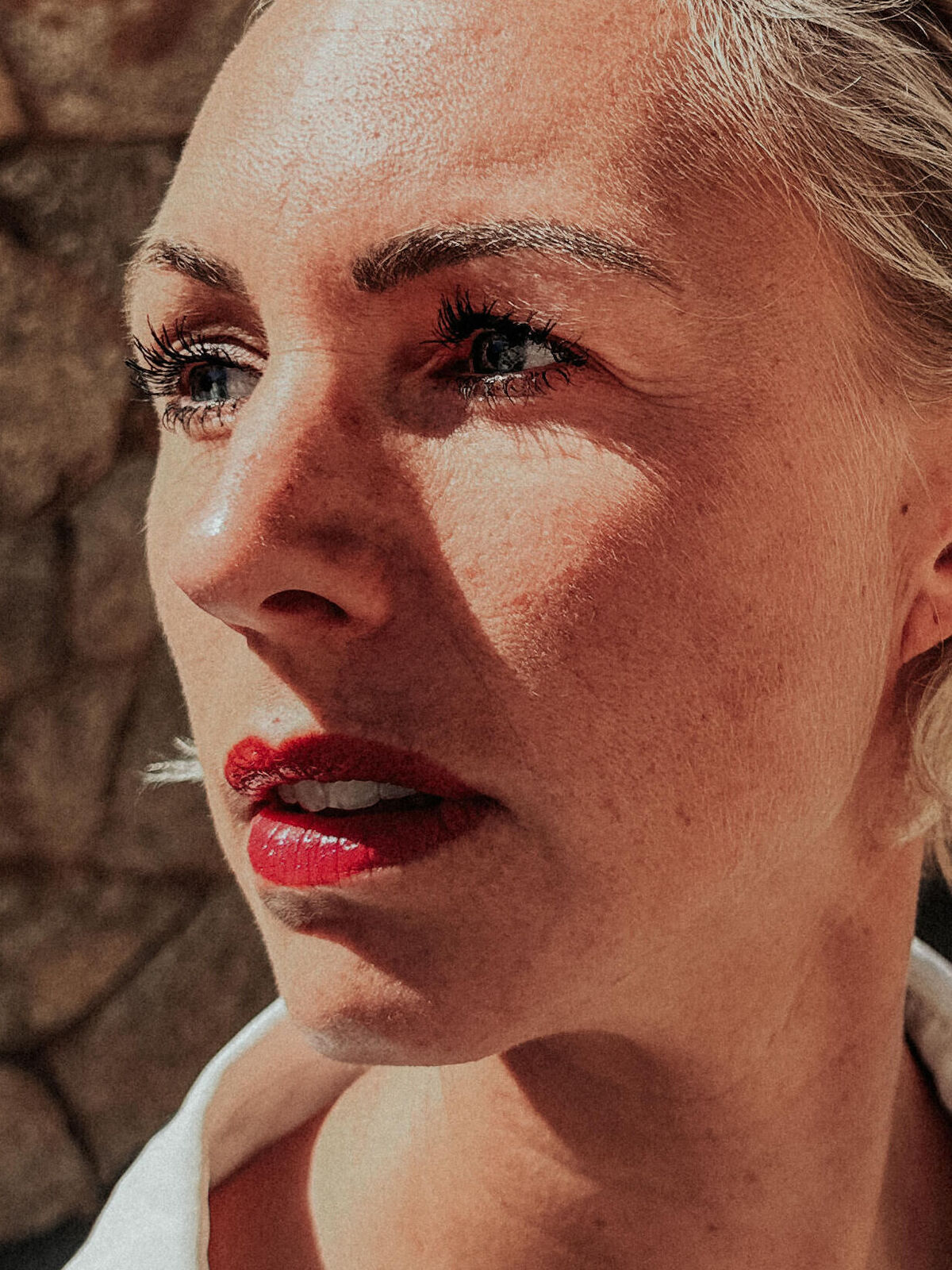 Eine Person steht draußen und lächelt mit Sonne im Hintergrund.