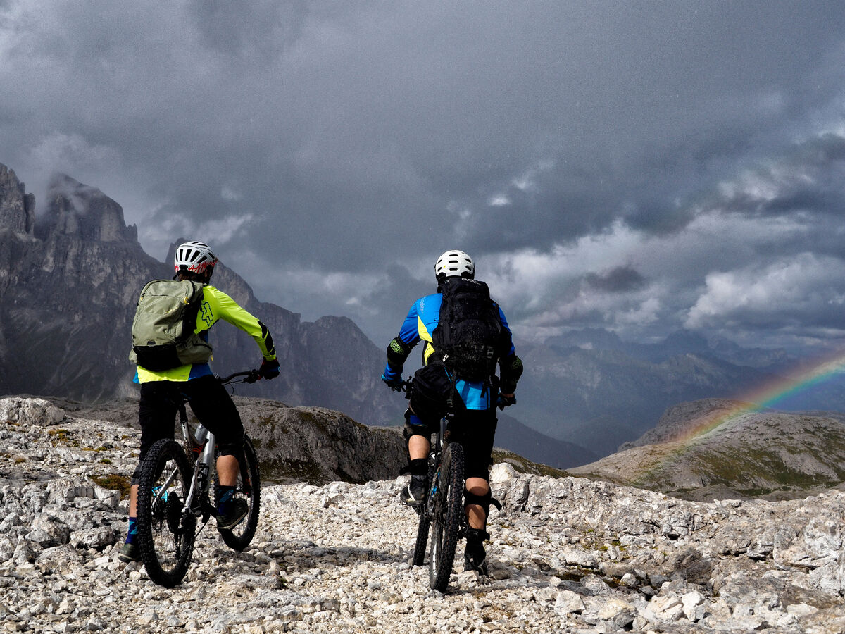 Zwei Radfahrer genießen die Aussicht in einem Gebirge unter einem Regenbogen