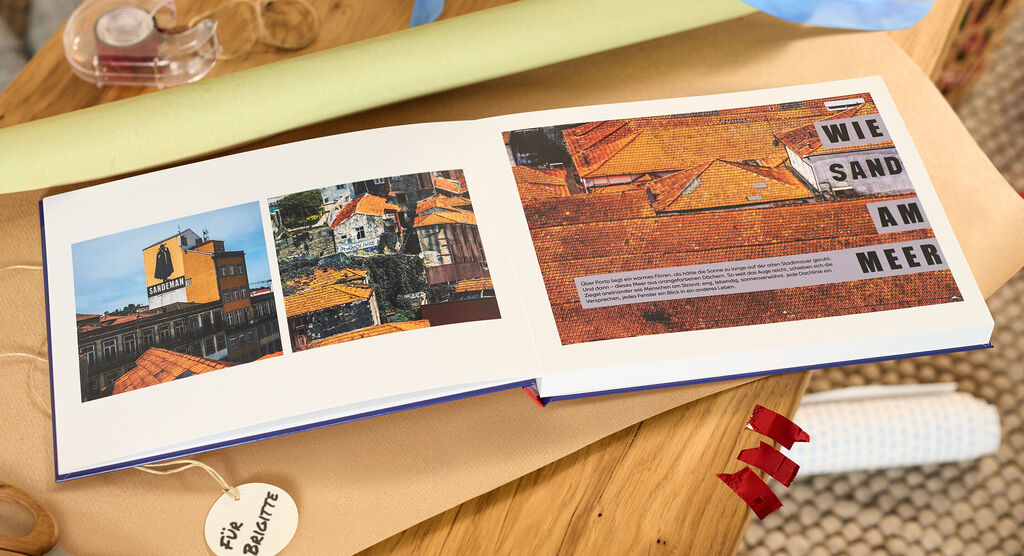 Offenes CEWE FOTOBUCH mit orangefarbenen Hausdächern und dem Text wie Sand am Meer.