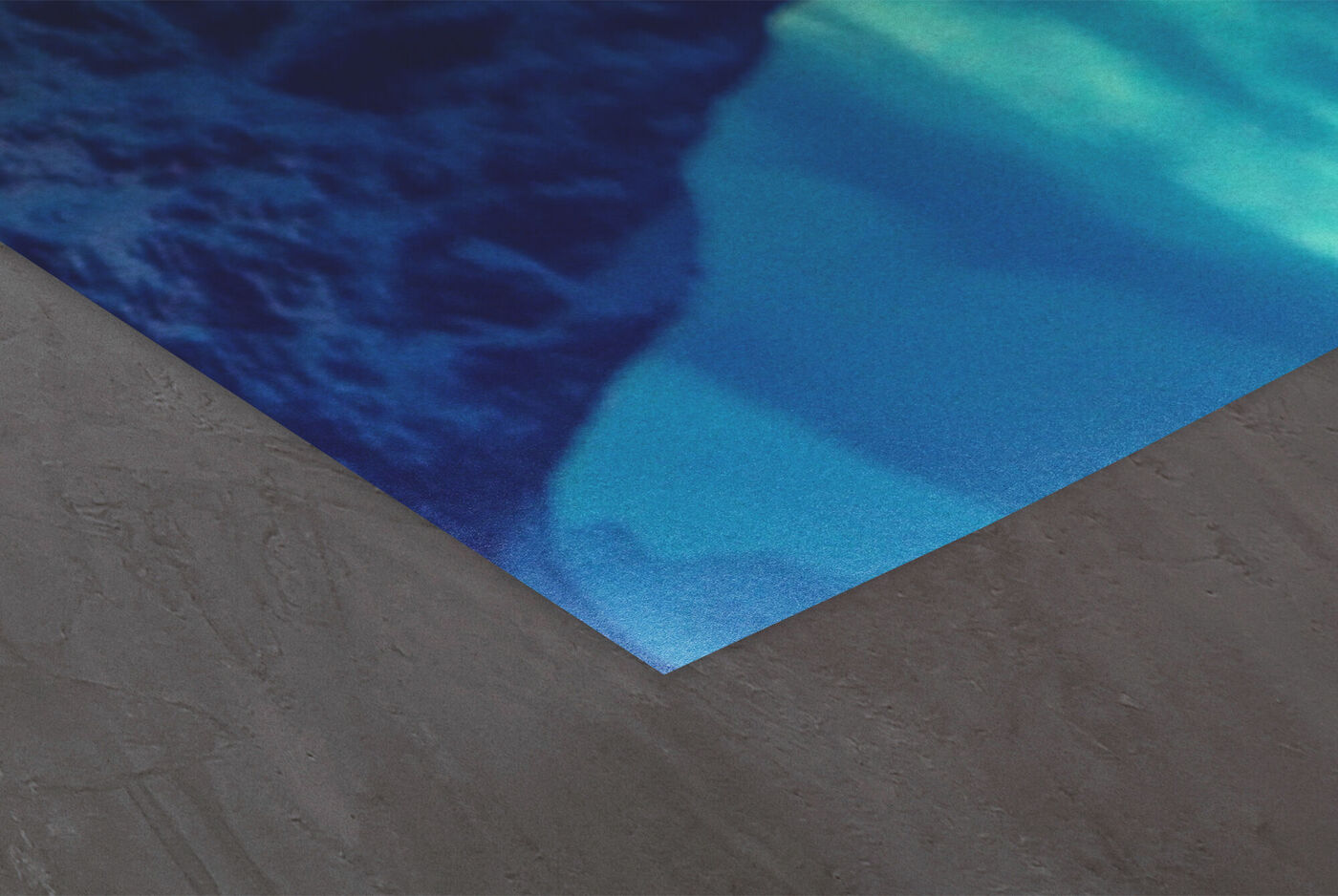 Ecke eines CEWE Posters mit blauem Fotomotiv auf grauem Untergrund