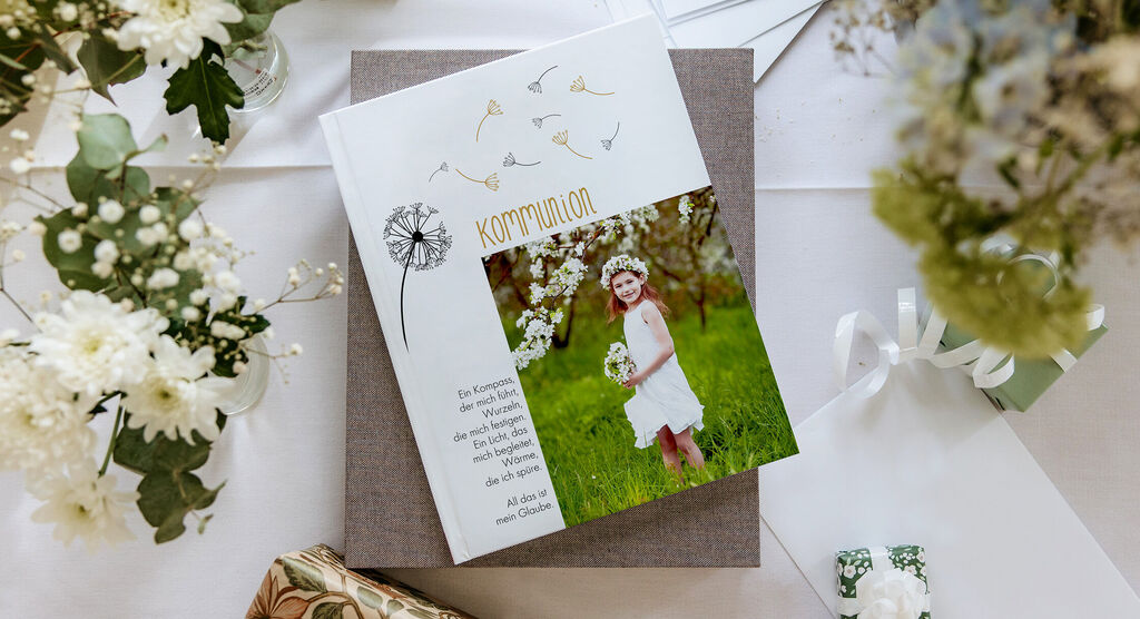 Ein wunderschönes CEWE Fotobuch zur Kommunion liegt auf einer feierlichen Tischdeko mit Blumen und Geschenken.