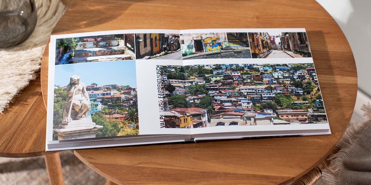 Aufgeschlagenes CEWE Fotobuch mit bunten Bildern von Reisemomenten auf einem Tisch