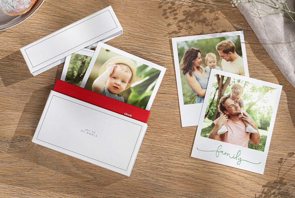Eine Auswahl schöner Familienfotos in einer CEWE Fotokarte, die gemütlich auf einem Holztisch liegen.