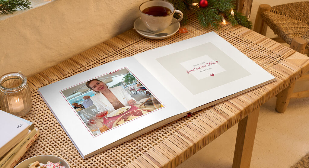 Ein liebevoll gestaltetes Fotobuch auf einem Tisch, umgeben von einer Tasse Tee und Weihnachtsdekoration.