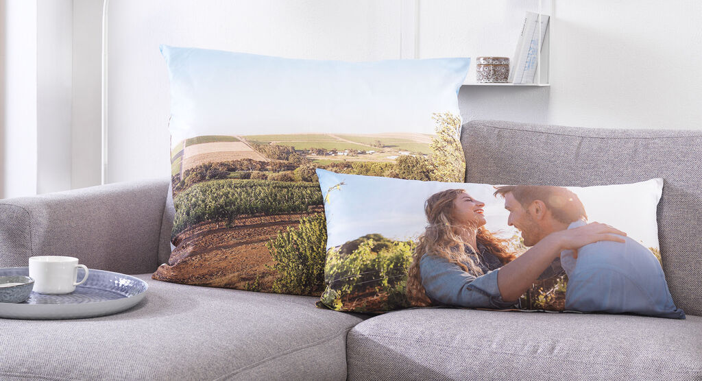 Zwei Kissen mit Landschafts- und Pärchenmotiv auf einem Sofa.