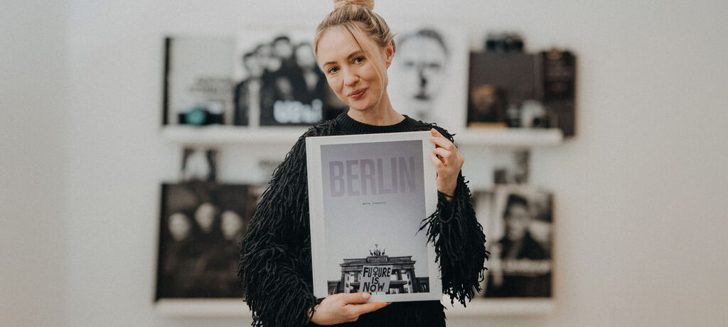 Marta Urbanelis steht vor ihrer Bücherwand und hält ein CEWE FOTOBUCH mit dem Titel "Berlin" in den Händen.