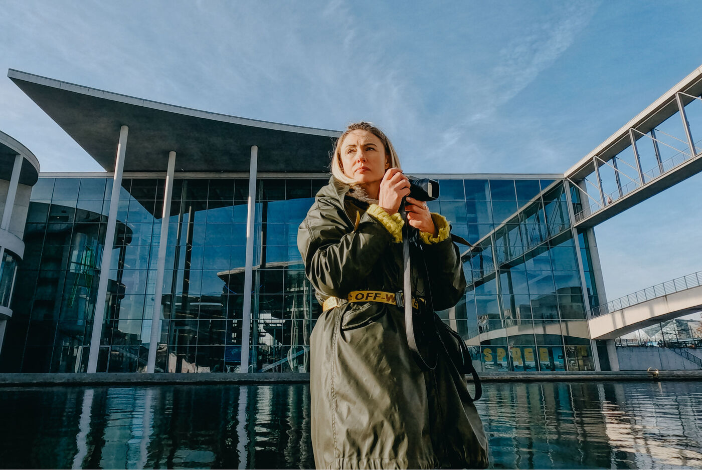 Frau mit Kamera vor einem modernen Glasgebäude