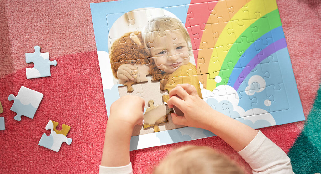 Ein Kind puzzelt ein farbenfrohes Puzzle mit einem Regenbogen und Wolken. Es ist ein schöner Moment des Spielens und Lernens.