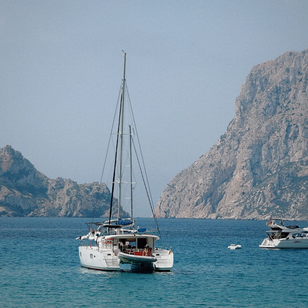 Segelboot und Motorboot auf türkisfarbenem Meer vor felsiger Küste und Bergen.