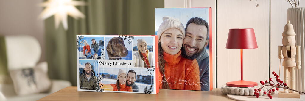 Zwei CEWE Fotobücher mit weihnachtlichem Design stehen auf einem Holztisch, umgeben von gemütlicher Einrichtung.