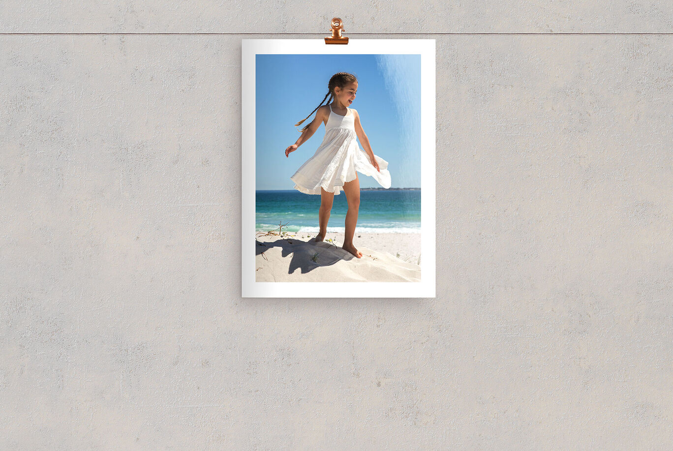 Ein fröhliches Mädchen in einem weißen Kleid, das am Strand steht, umgeben von Sand und Meer unter blauem Himmel.