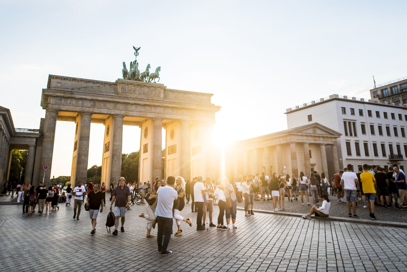 Das Brandenburger Tor in Berlin bei Sonnenuntergang mit vielen Menschen auf dem Platz.