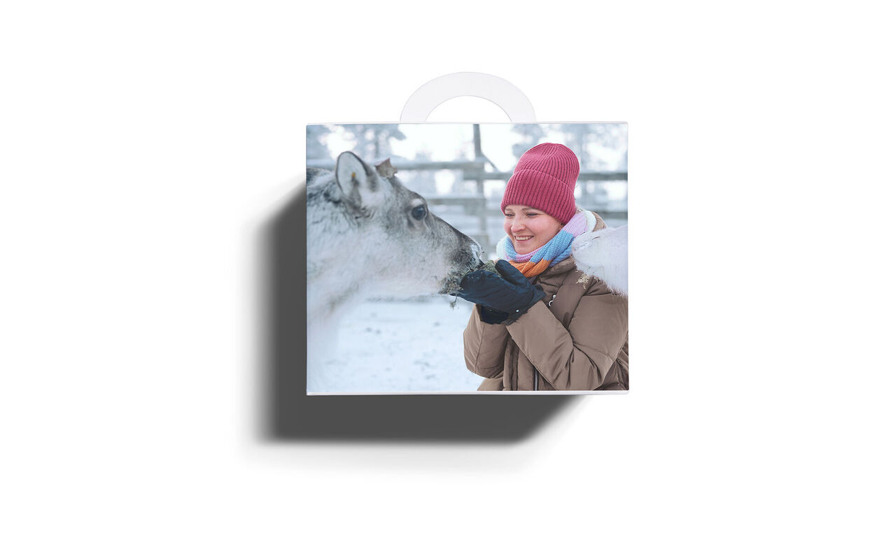 CEWE Adventskalender Geschenkbox mit Foto von Person mit roter Mütze, die ein Rentier im Schnee füttert