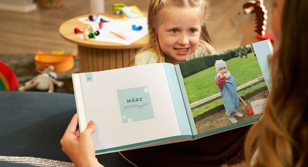 Mutter und Kind betrachten ein geöffnetes CEWE FOTOBUCH mit einer Märzseite und einem Foto des Kindes im Garten.