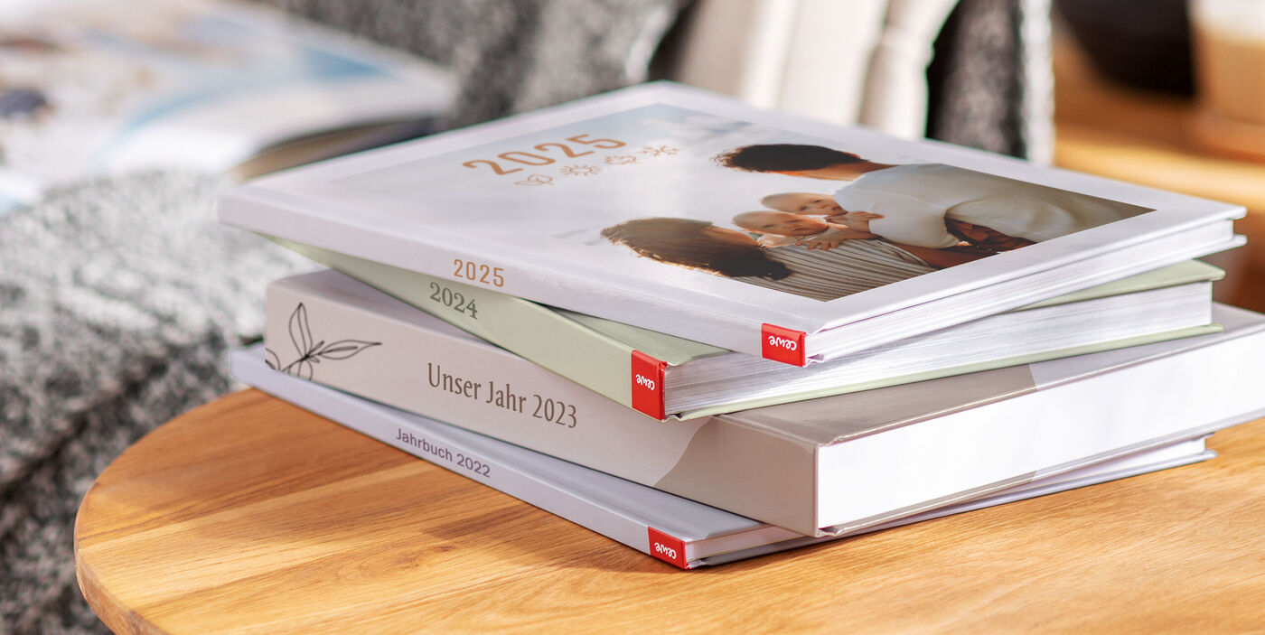 Vier CEWE FOTOBÜCHER mit Jahreszahlen liegen gestapelt auf einem Holztisch