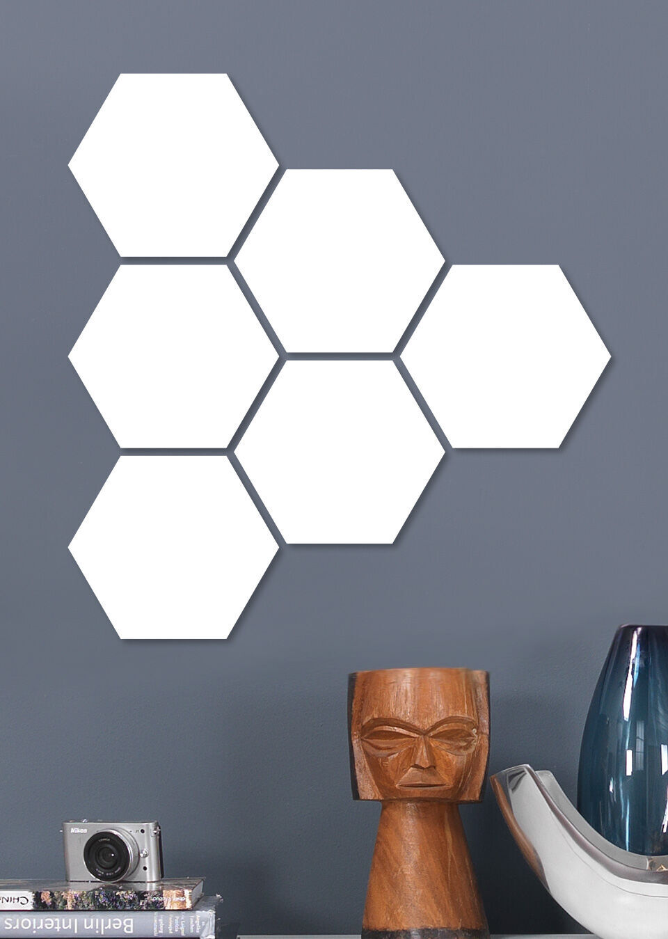 Sechs weiße Hexagon-Formen an einer grauen Wand, daneben eine moderne Lampe und eine Kamera