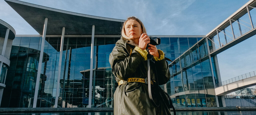 Frau mit Kamera vor einem modernen Glasgebäude