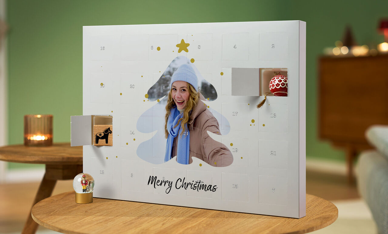 Ein geöffneter Adventskalender in Form eines Weihnachtsbaums mit Geschenken und der Aufschrift 'Merry Christmas' in einem gemütlichen Raum