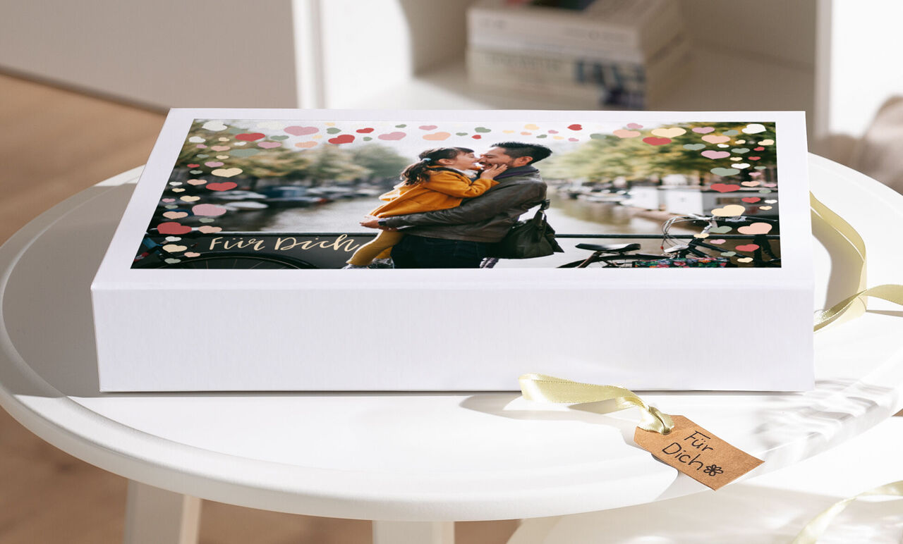 Geschenkbox mit süßem Design, darin ein Pärchen küsst sich vor einer romantischen Kulisse