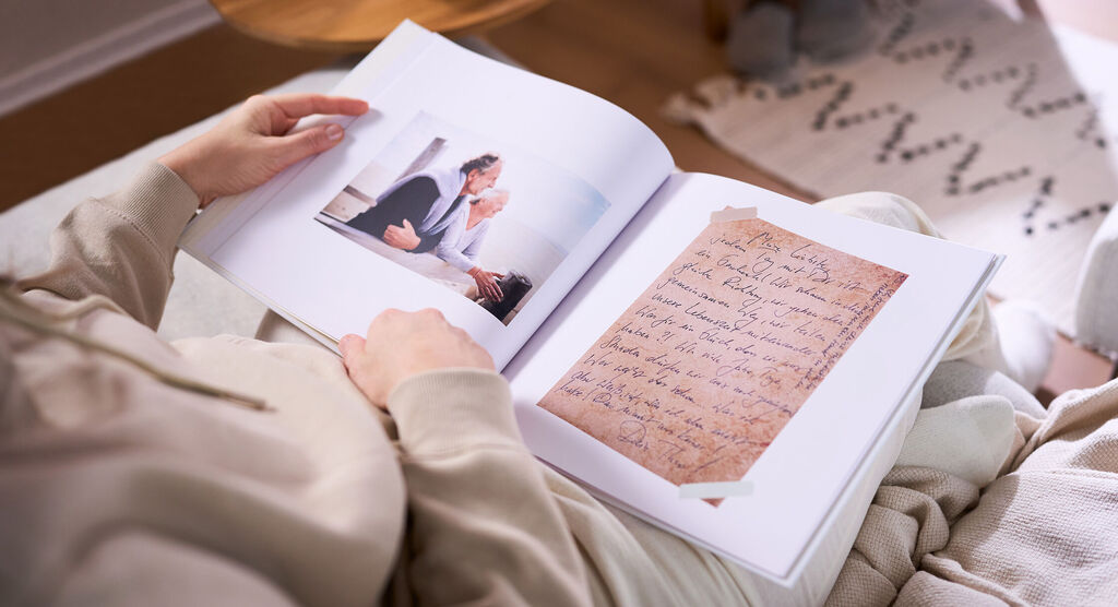 Eine Frau hält in ihren Händen ein aufgeschlagenes CEWE FOTOBUCH, das ein großes Foto und einen eingescannten Brief zeigt.