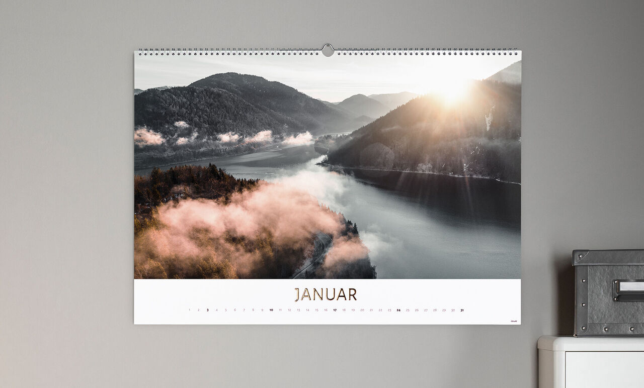 Ein CEWE Fotokalender zeigt die Ansicht eines Flusses und Berge im Januar mit sanftem Sonnenlicht.