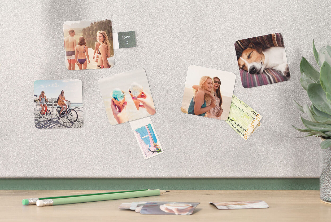 Bunte Fotokarten mit Urlaubserinnerungen hängen an einer grauen Wand, darunter liegen weitere Bilder