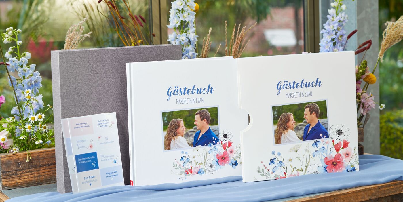 Zwei Hochzeitsgästebücher als CEWE FOTOBUCH mit Paarfoto und Blumen, Text 'Gästebuch', dazu graue Box und Karten