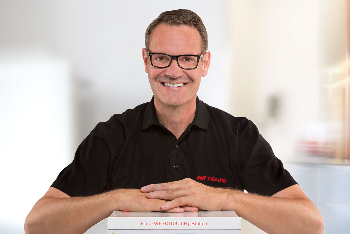 Ein fröhlicher Mann hält ein CEWE FOTOBUCH vor seinem Körper und lächelt.