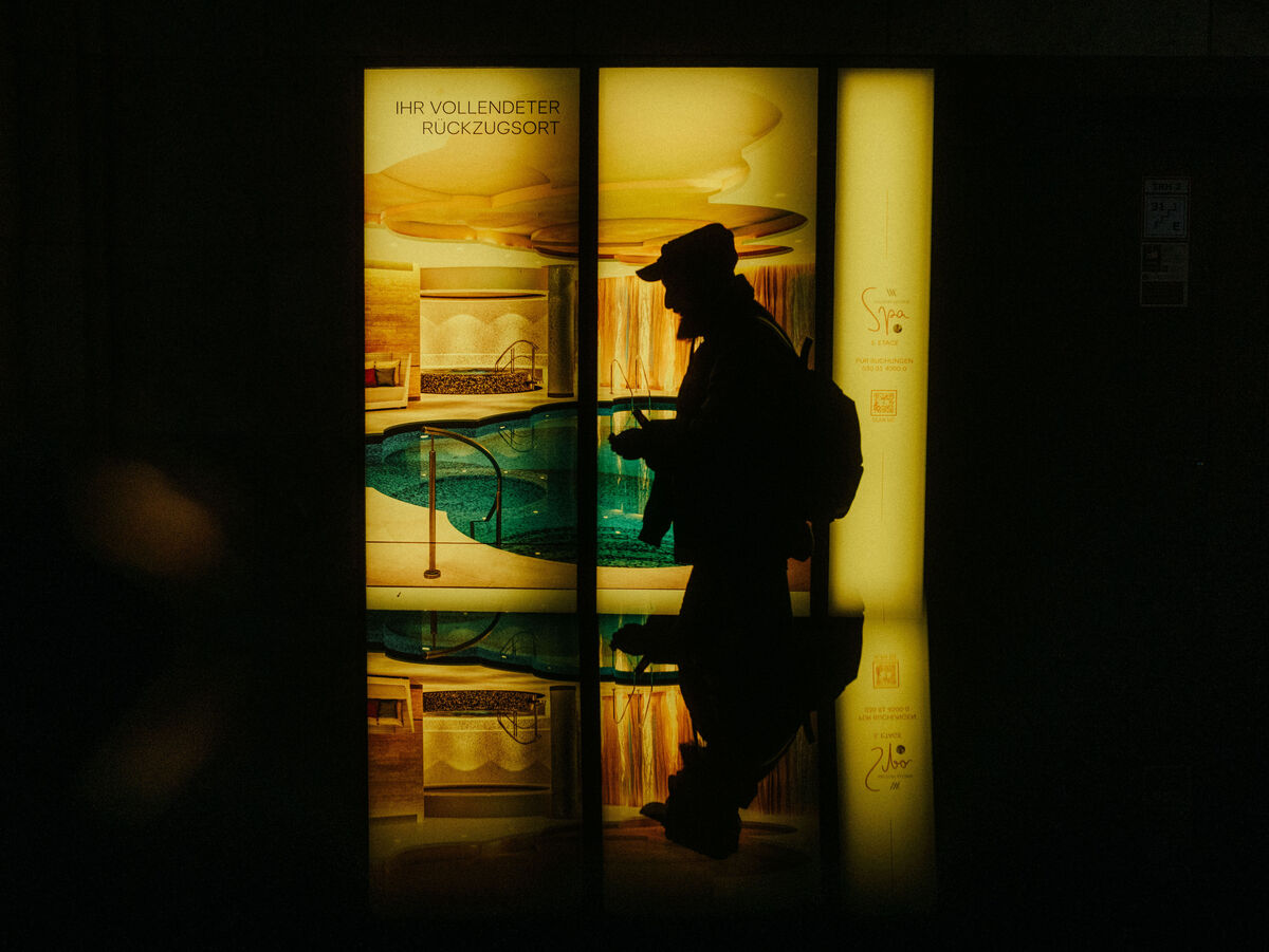 Dunkle Silhouette einer Person vor warm gelb leuchtenden Fenstern mit Spiegelung auf dem Boden