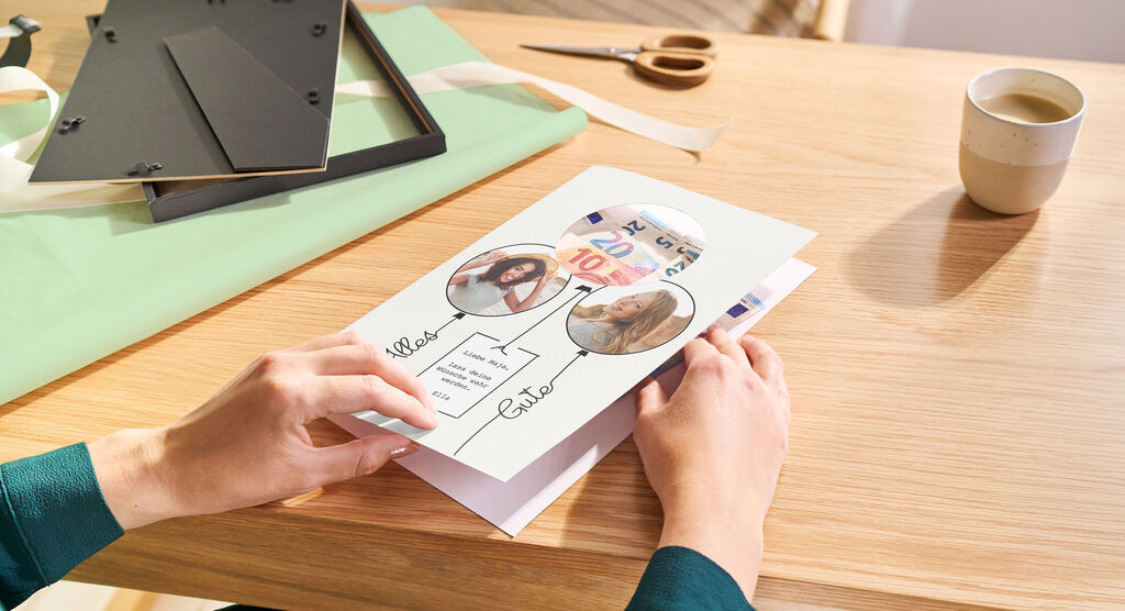Hände halten eine gestaltete Karte mit zwei Fotos und Text auf einem Tisch