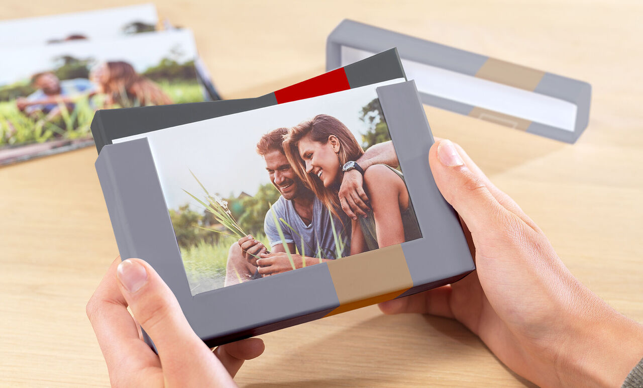 Eine Person hält ein Fotobuch mit einem wunderschönen Bild in den Händen. Im Hintergrund sind weitere Fotobücher zu sehen, die emotionale Momente teilen.