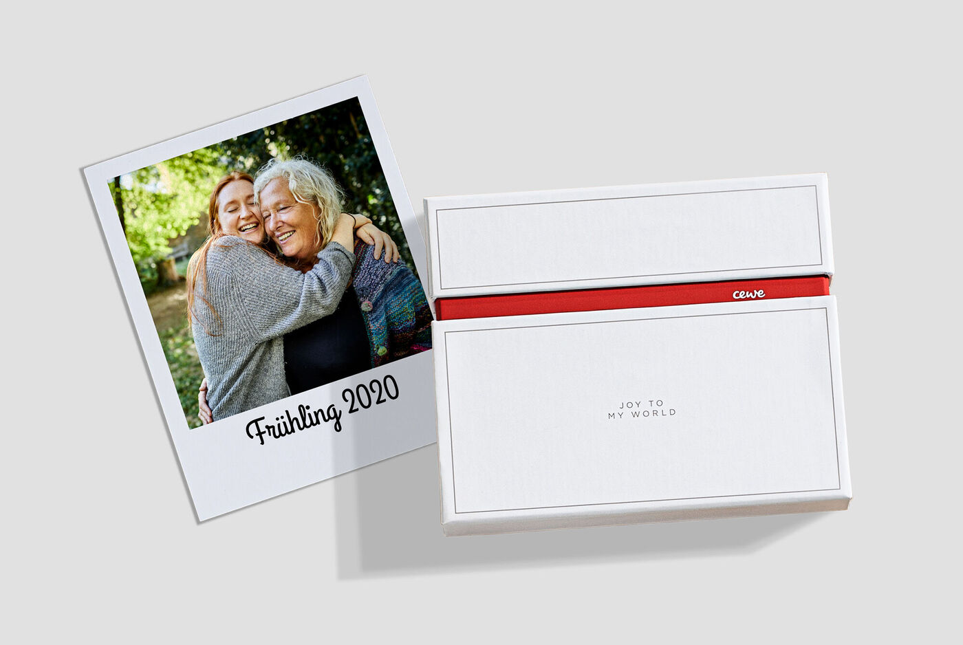 Ein liebevolles Foto von zwei Menschen, die sich umarmen, daneben eine personalisierte CEWE Geschenkbox mit rotem Band.