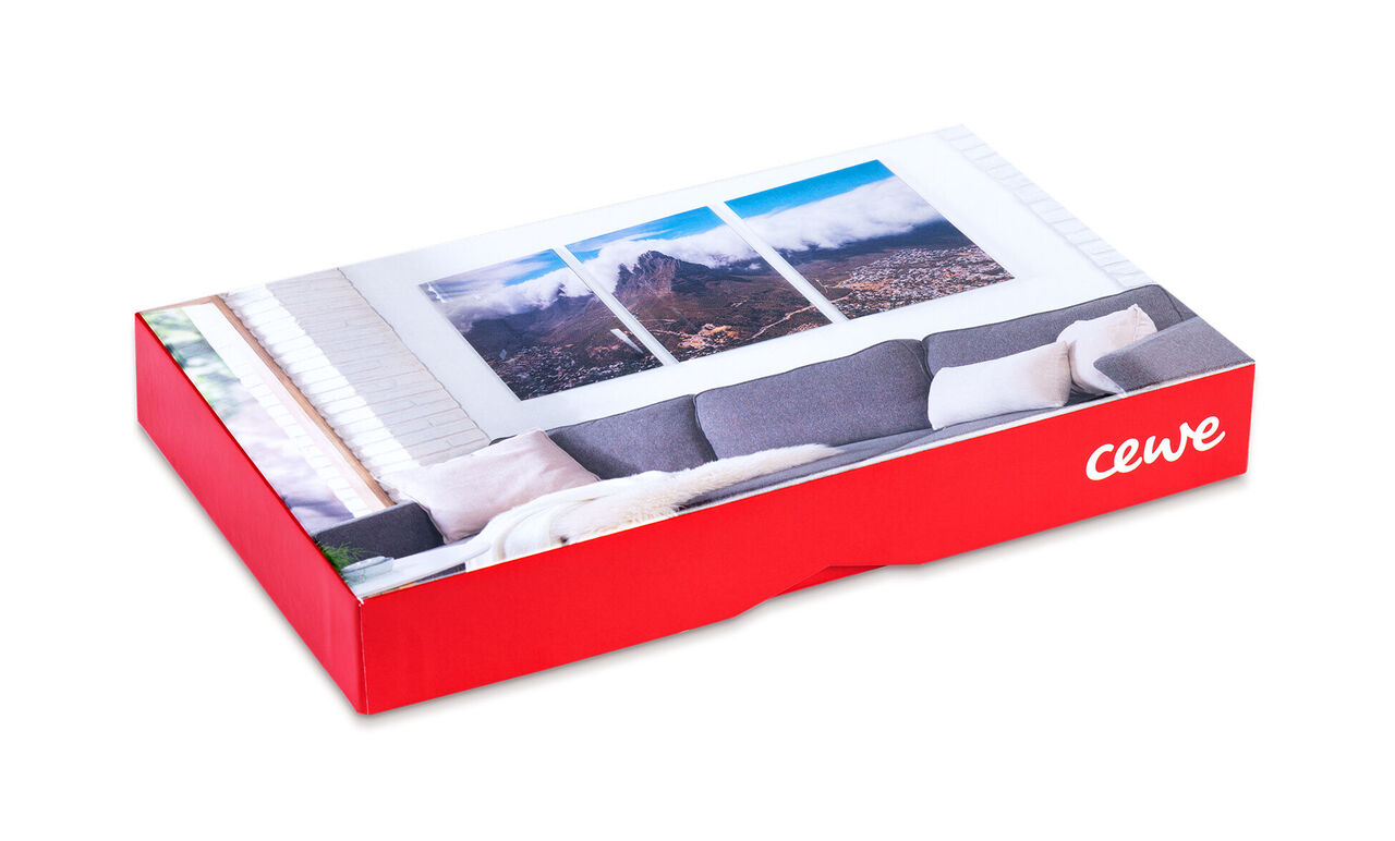 CEWE Fotobuch in einer roten Verpackung, das auf einem grauen Sofa liegt.