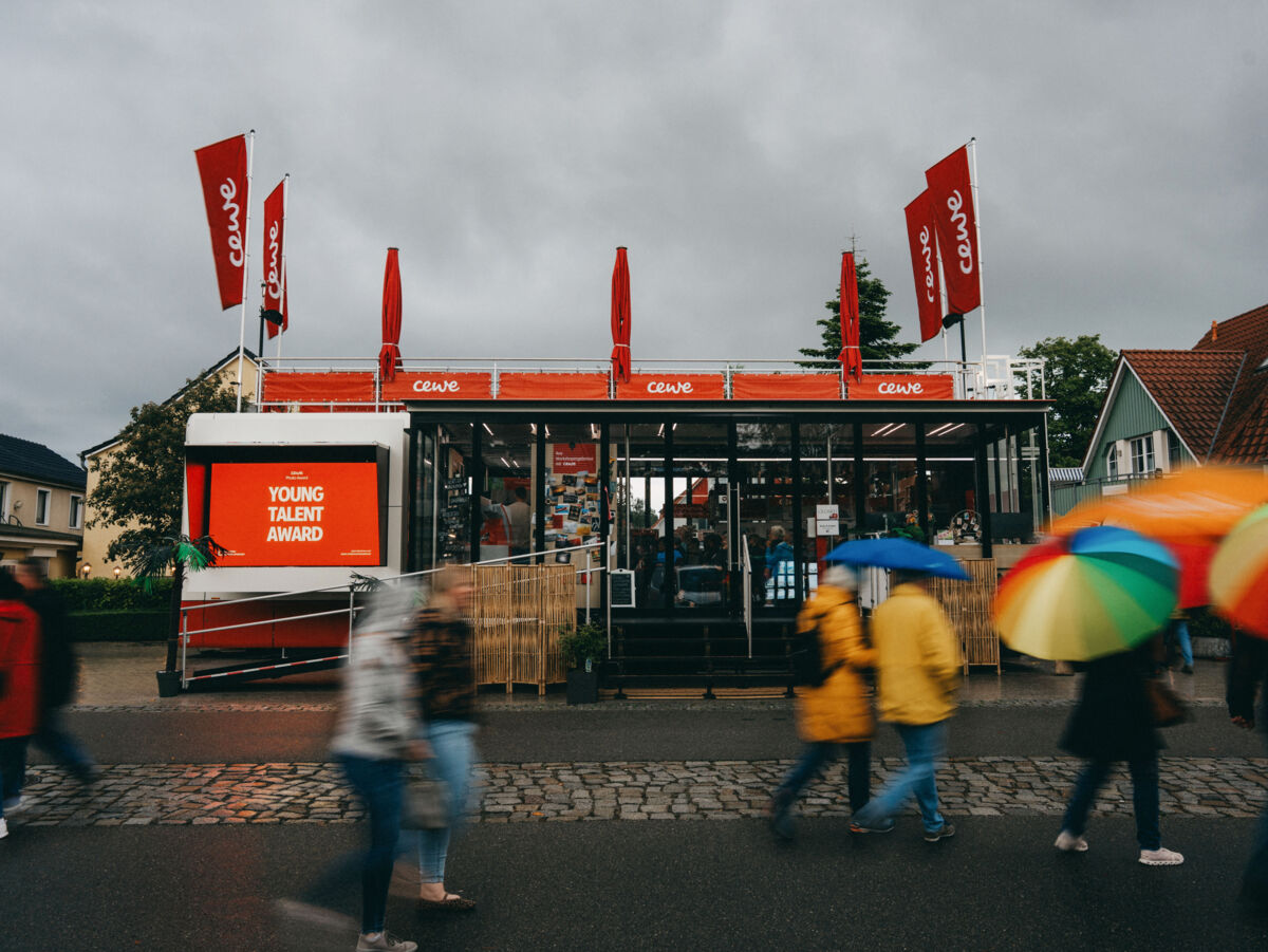 Der CEWE Truck steht bei Regen in der Einkaufsstraße. Im Vordergrund sind viele Passanten mit bunten Regenschirmen in Bewegung aufgenommen.