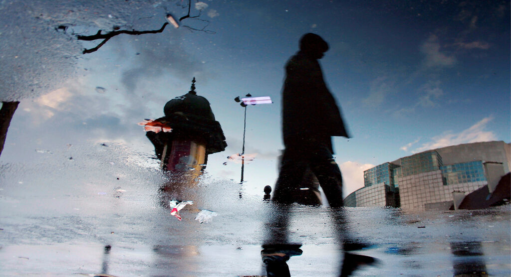 Silhouette eines Spaziergängers auf nasser Straße mit reflektierenden Wolken und Gebäuden
