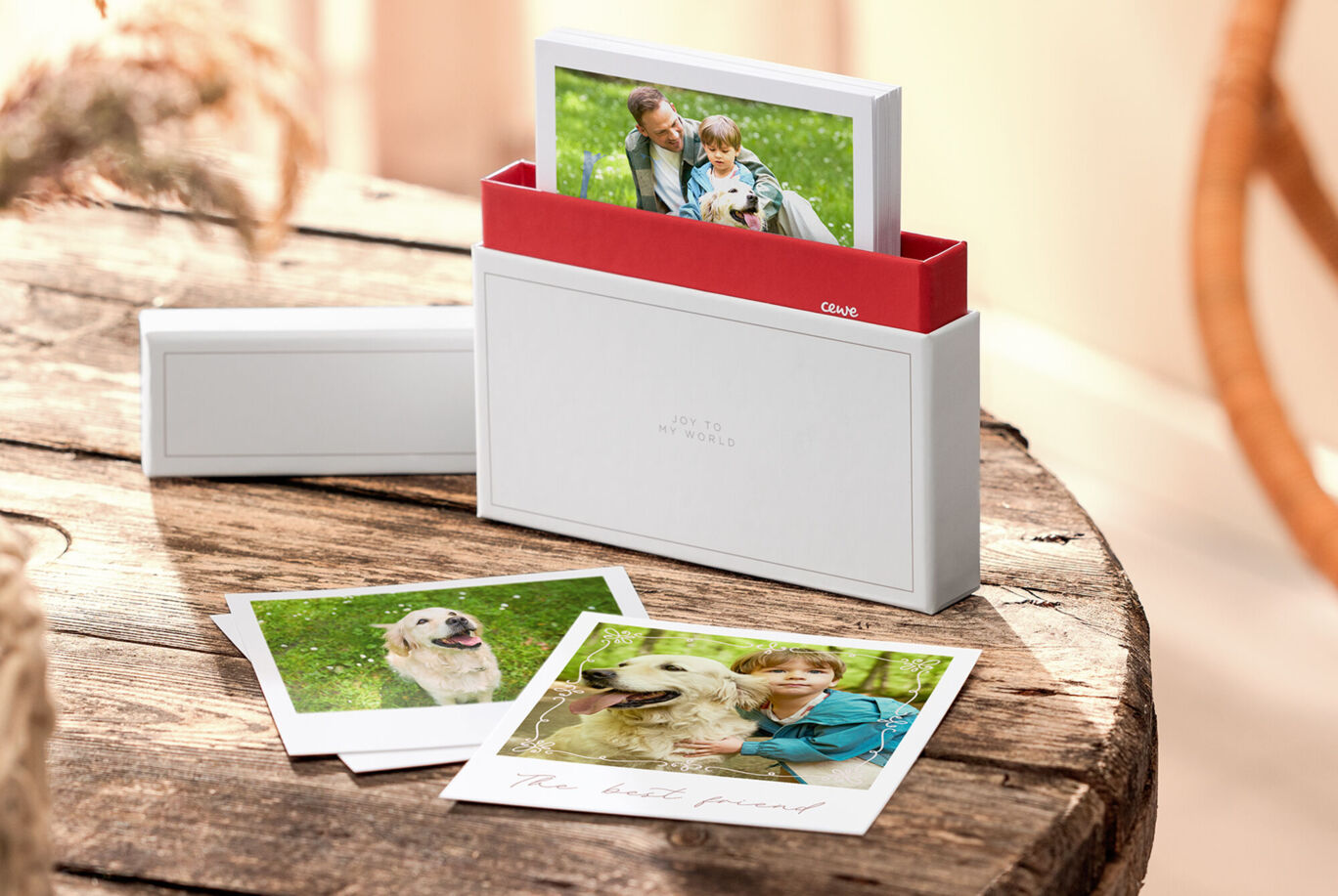 Auf einem Holztisch stehen eine Fotoaufbewahrungsbox und mehrere Sofortbild‑Fotos mit Menschen.