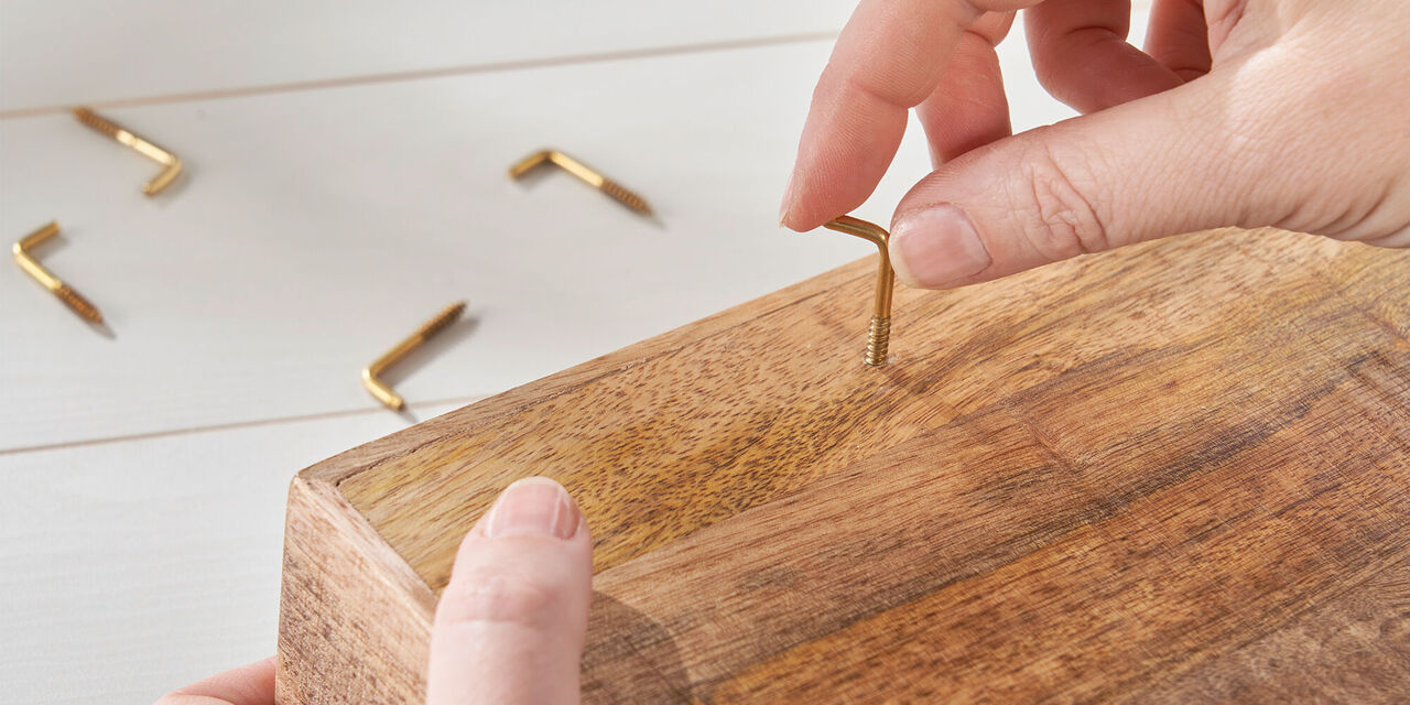 Eine Person bringt einen goldenen Schraubenkopf in ein Holzbrett ein