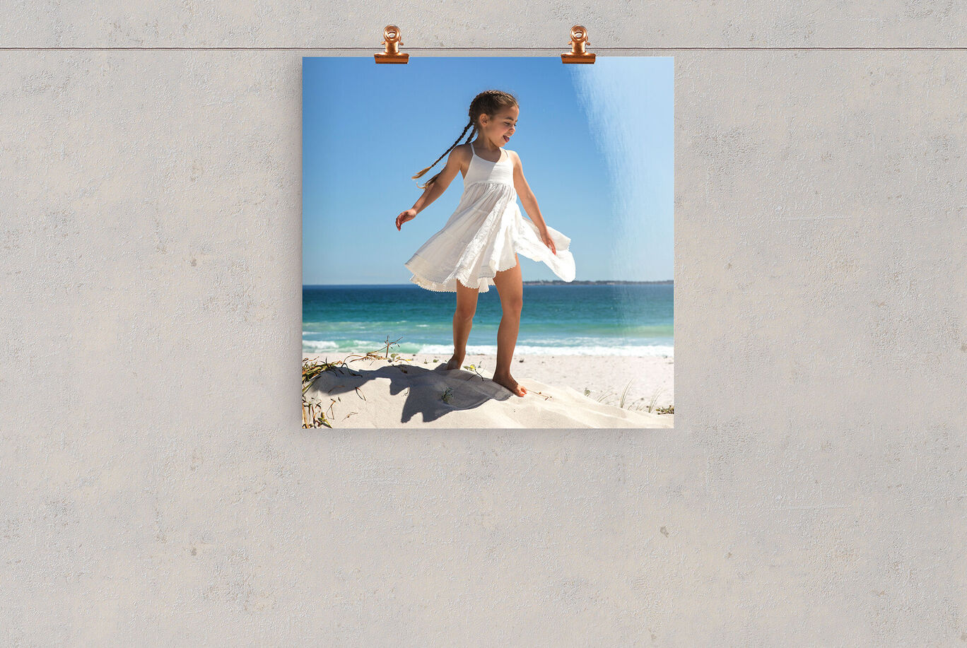 Ein fröhliches Kind in einem weißen Kleid steht am Strand und genießt den Wind.