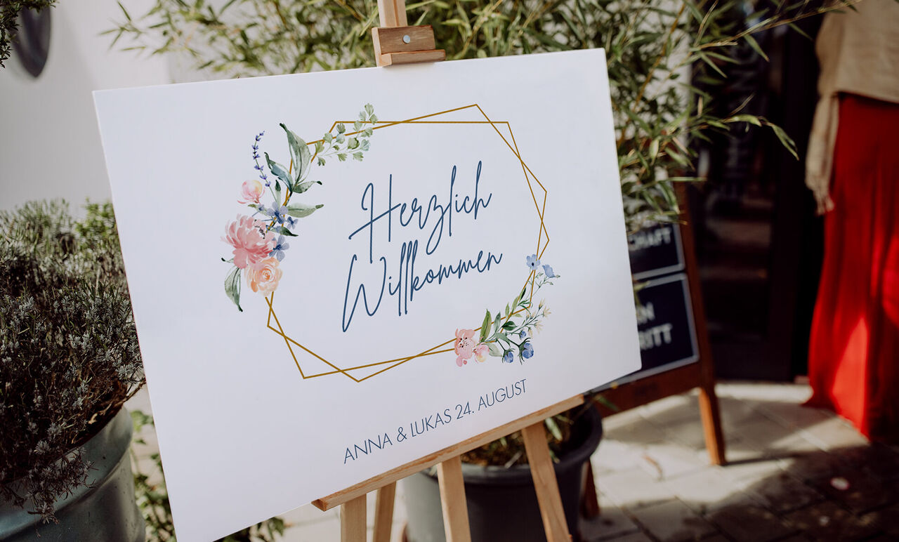 Ein Willkommensschild mit Blumenrahmen und handschriftlichem Text.