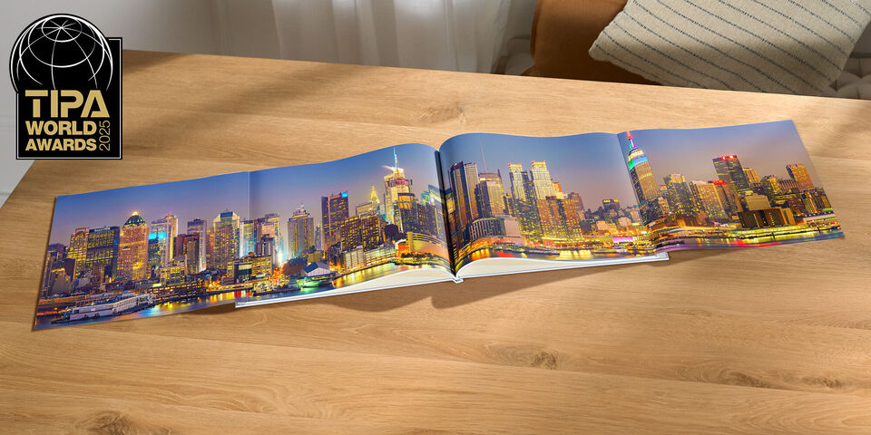 Ein geöffnetes CEWE FOTOBUCH auf einem Holztisch, zeigt eine wunderschöne Stadtansicht bei Nacht mit bunten Lichtern.