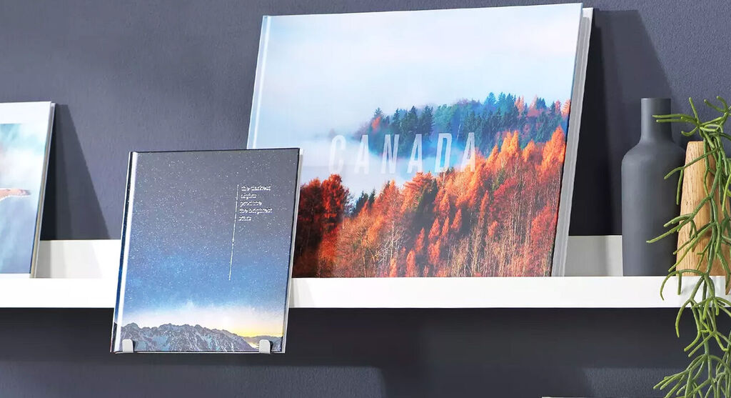 Auf einem Wandregal stehen mehrere Fotobücher. Auf einem ist eine kanadische Landschaft zu sehen, auf einem anderen ein Sternenhimmel.