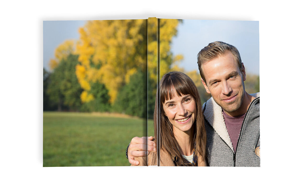 Ein Paar hält ein Fotobuch in einem grünen Park, umgeben von herbstlichen Bäumen