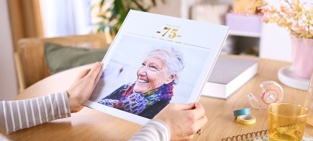 Eine Frau sitzt an einem Tisch, in ihren Händen hält sie ein CEWE FOTOBUCH. Auf dem Cover ist ein Foto einer Frau zu sehen.