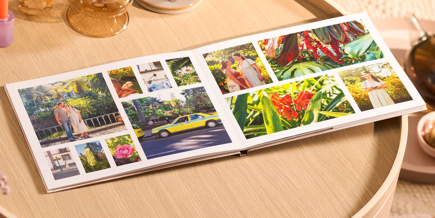 Offenes CEWE FOTOBUCH auf rundem Holztisch mit vielen bunten Reisefotos in verschiedenen Größen.