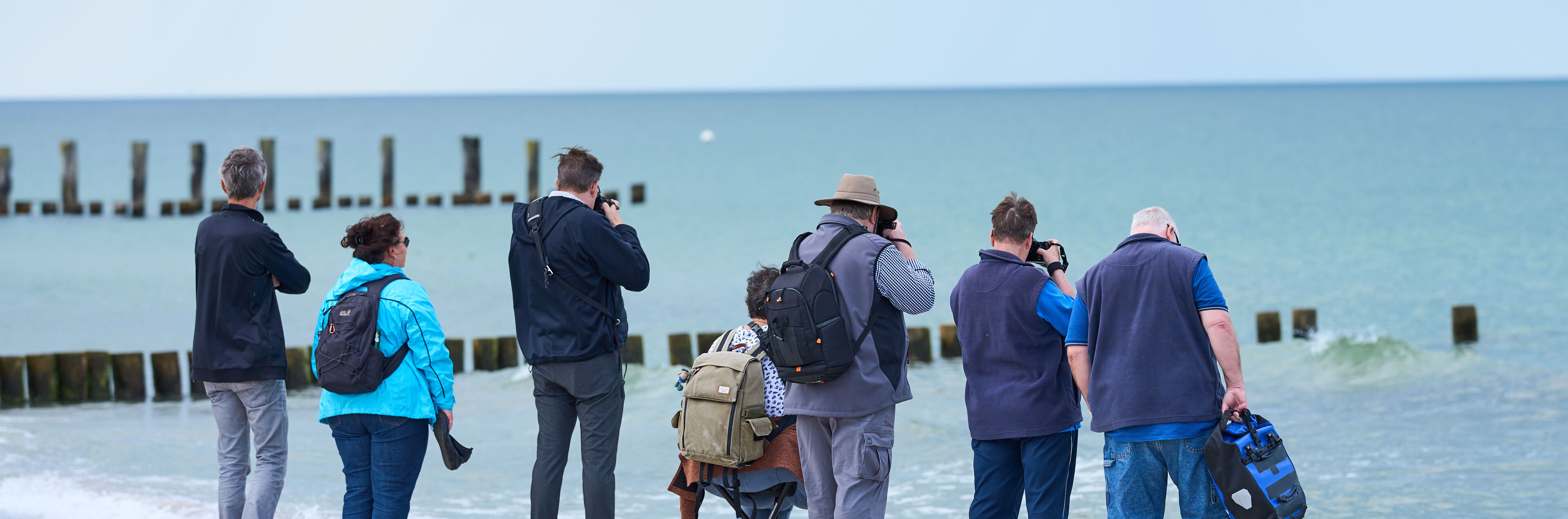 Eine Gruppe von Fotografen steht am Strand und fotografiert das Meer.