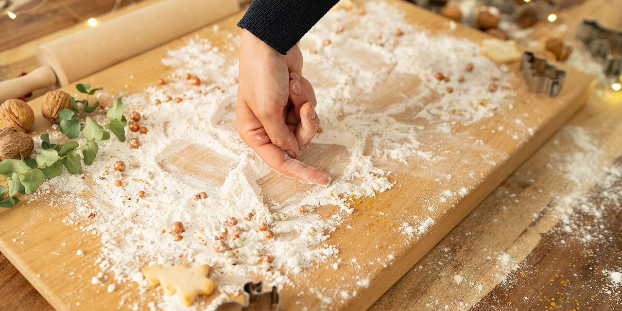 Eine Person formt einen Teig auf einer Holzplatte mit Mehl und Nüssen für Plätzchen.