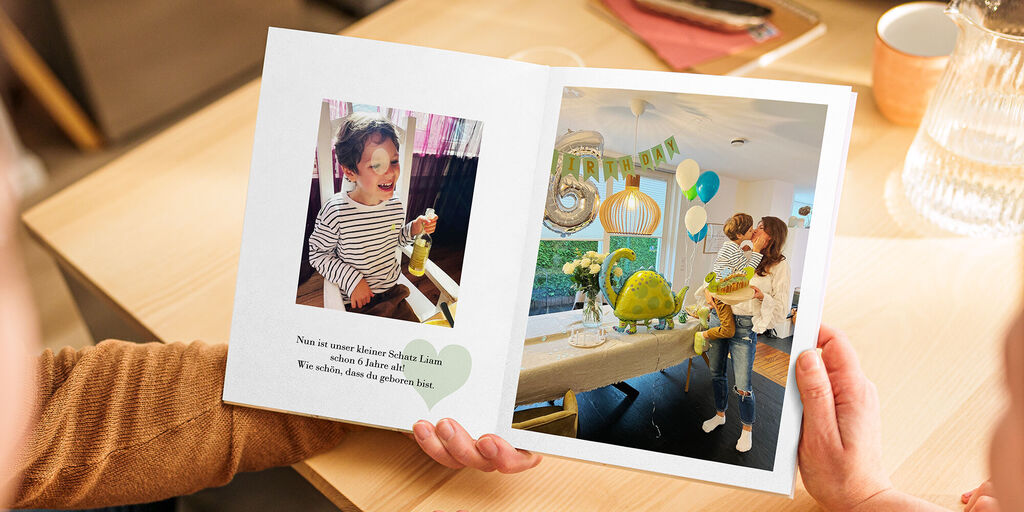 Ein offenes CEWE FOTOBUCH zeigt eine fröhliche Feier mit Dekoration und zwei Personen, die schöne Momente teilen
