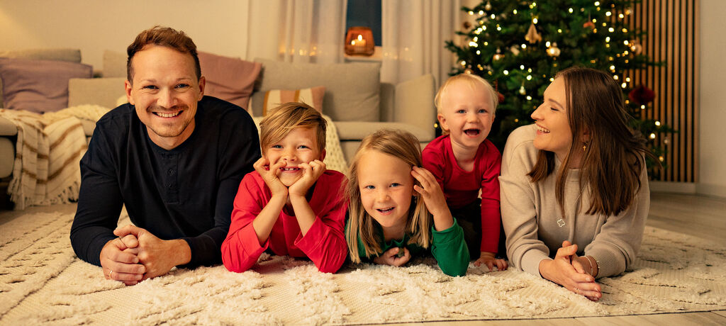 Fünf Kinder und ein Erwachsener liegen entspannt auf einem Teppich, umgeben von weihnachtlicher Dekoration und einem festlichen Baum.