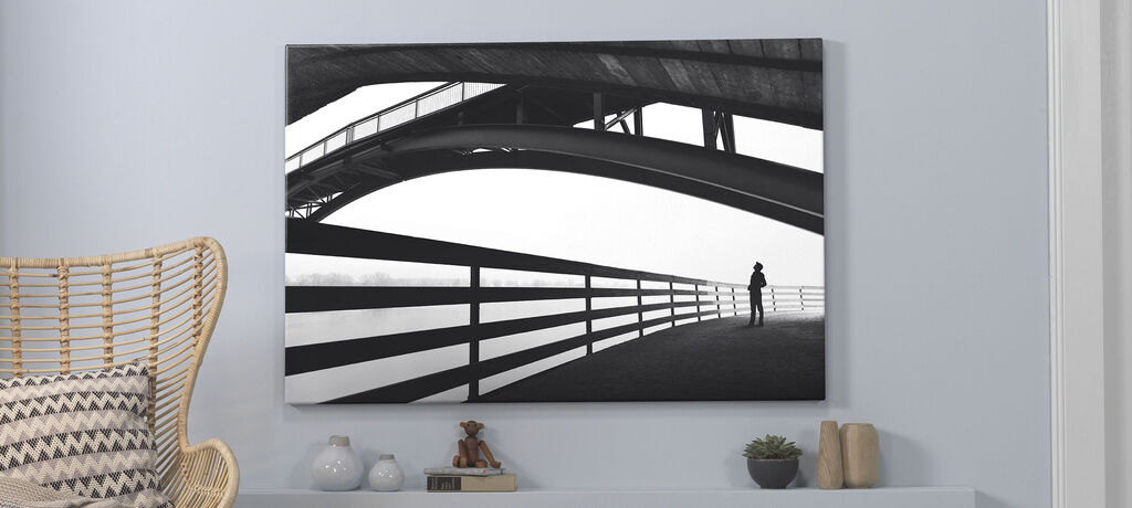 Dunkles Wandbild eines stilisierten Brückenbogens mit einer silhouettierenden Person an der Seite wiedergegeben. Es strahlt Ruhe und Moderne aus.